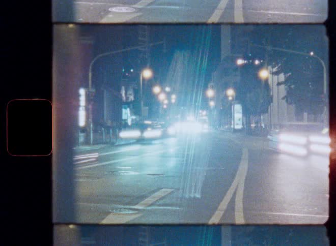 Vintage-style time-lapse shows glowing light trails from traffic on a busy city street at night