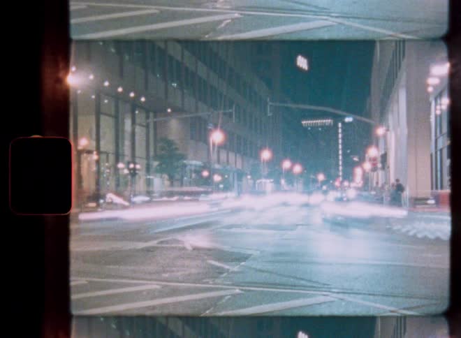 A vintage film time-lapse captures the mesmerizing light trails of traffic on a busy city street at night