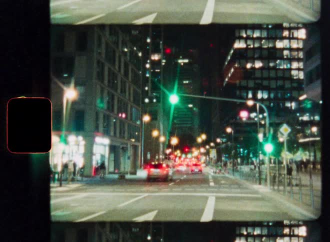 A vintage-style time-lapse of a bustling city intersection at night with traffic leaving light trails