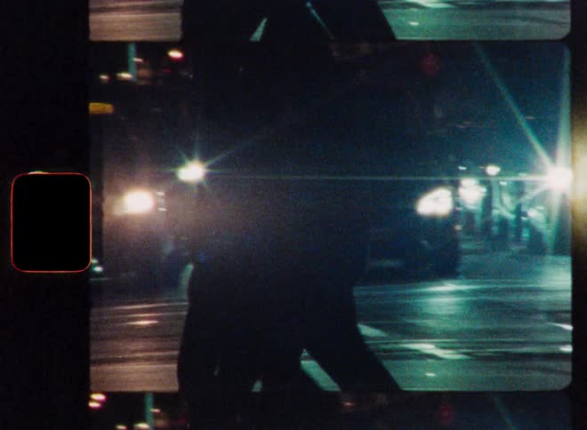Silhouetted pedestrians cross a busy urban street at night in this grainy, artistic Super 8 film footage