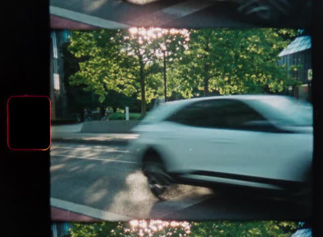 Vintage film scan shows city traffic speeding past with motion blur on a sunny day with light leaks