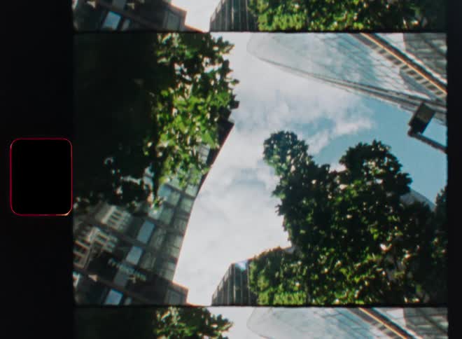 Stop-motion animation of a 35mm film strip revealing a low-angle shot of a sunny cityscape with modern skyscrapers