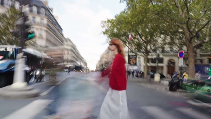 A fashionable woman in red stands out against the motion-blurred chaos of a busy street crossing in Paris