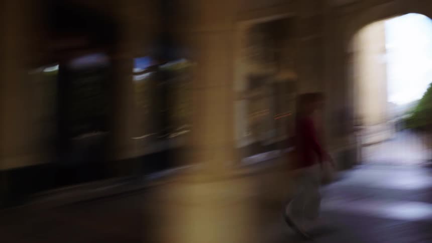 A stylish woman in a red sweater walks through a classic European colonnade in a dizzying, abstract, motion-blurred shot