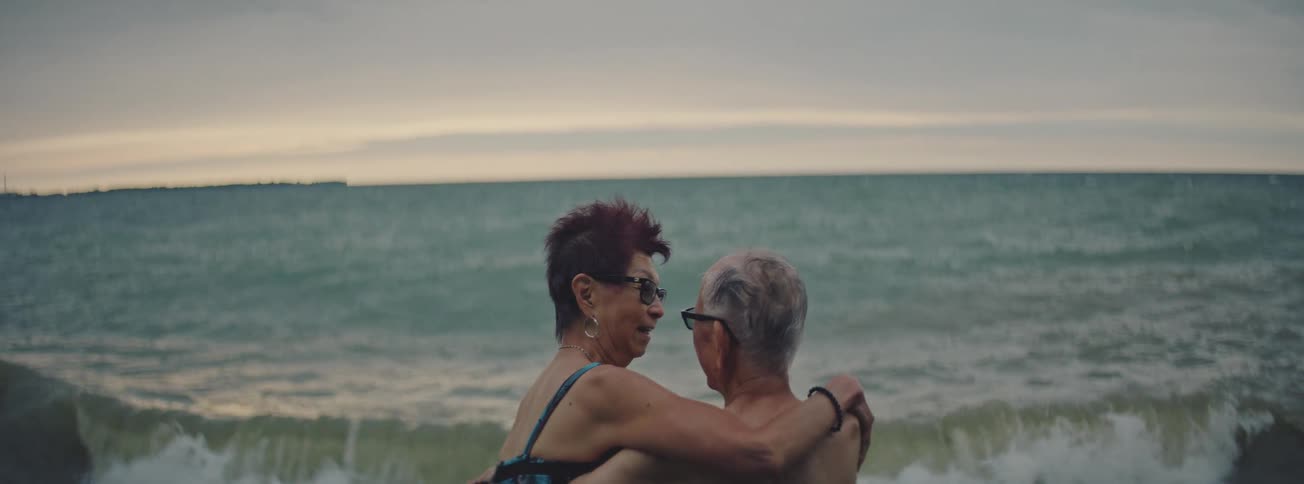 A romantic senior couple embraces while standing in the ocean on an overcast day