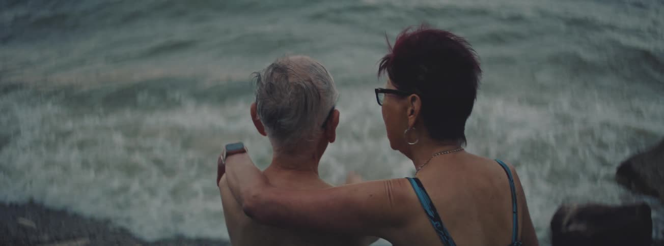 An intimate over-the-shoulder shot of a senior couple embracing as they watch the ocean waves roll in