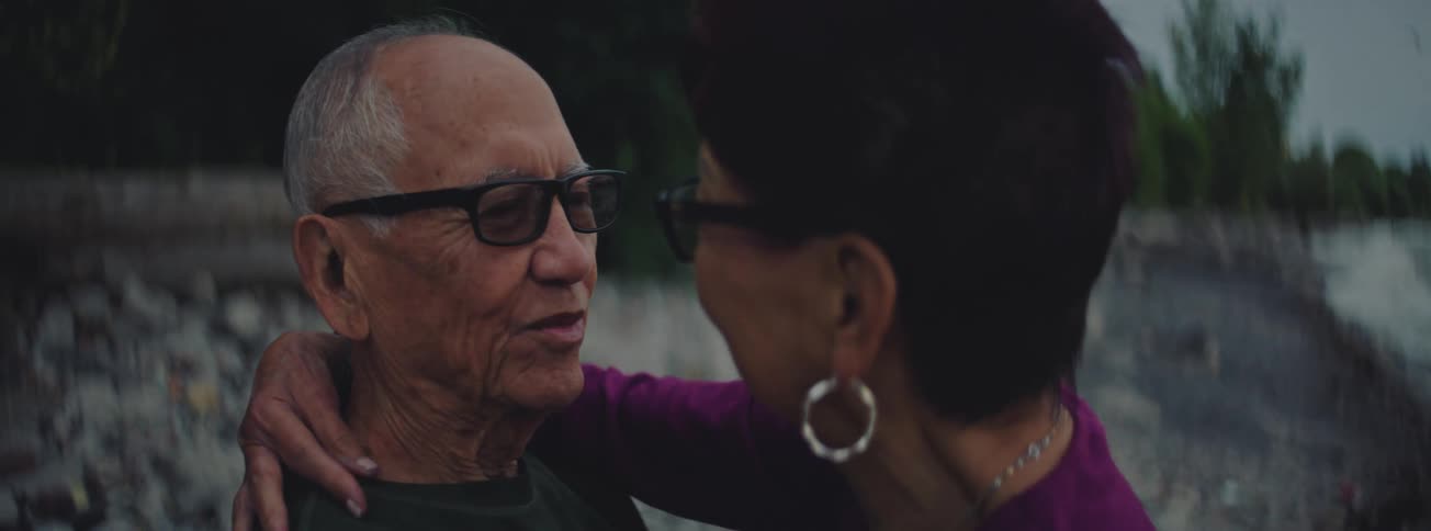 An elderly Asian couple shares a loving and intimate moment together outdoors in a slow-motion close-up