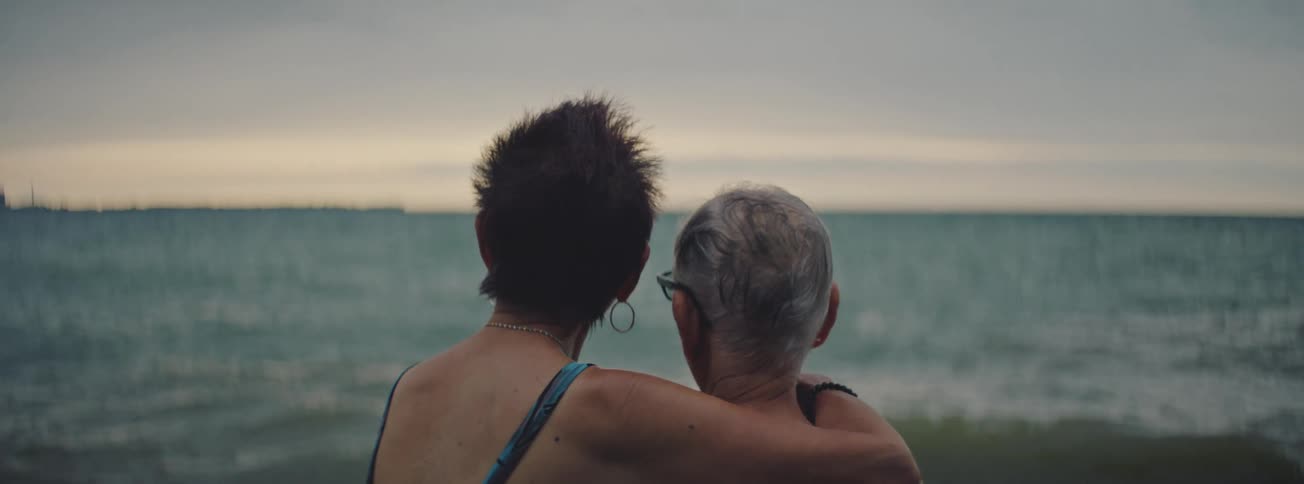 An intimate over-the-shoulder shot of a senior female couple embracing while watching the ocean waves