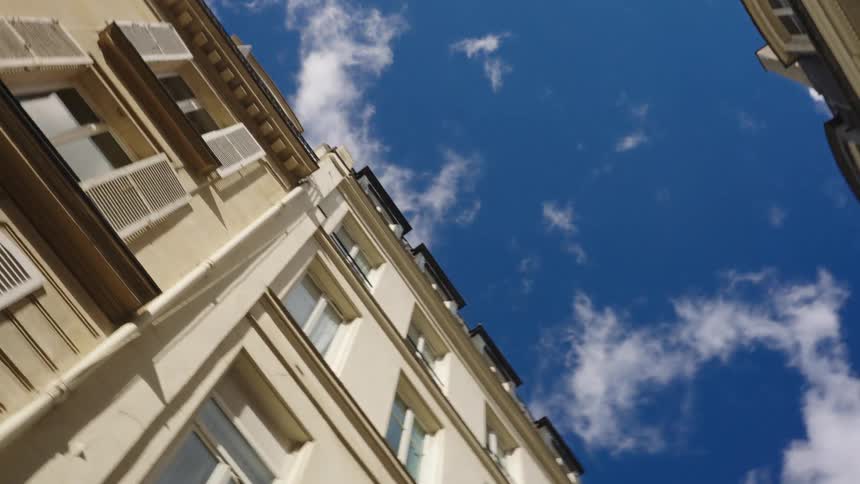 A rotating low-angle shot moves slowly down a narrow street, looking up at the sky between classic Parisian apartment buildings