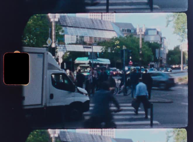 A vintage film time-lapse captures the bustling energy of a city street corner with pedestrians and traffic flowing through the intersection