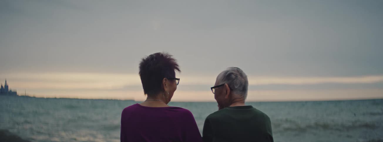 Rear view of a senior couple sitting together, talking and enjoying the view of the ocean at dusk