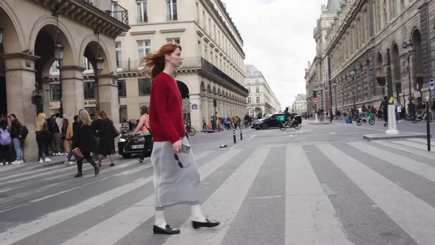 A stylish woman with red hair walks across a busy crosswalk in Paris in slow motion