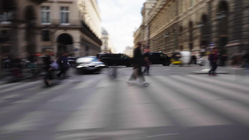 A motion blur time-lapse captures the fast-paced energy of pedestrians and traffic on a busy Parisian street