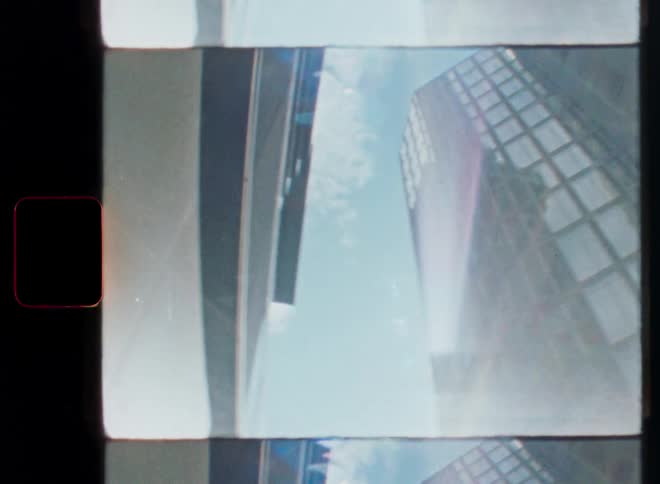 Stylized vertical shot of a Super 8mm film strip moving through the frame, showing a skyscraper from a low angle