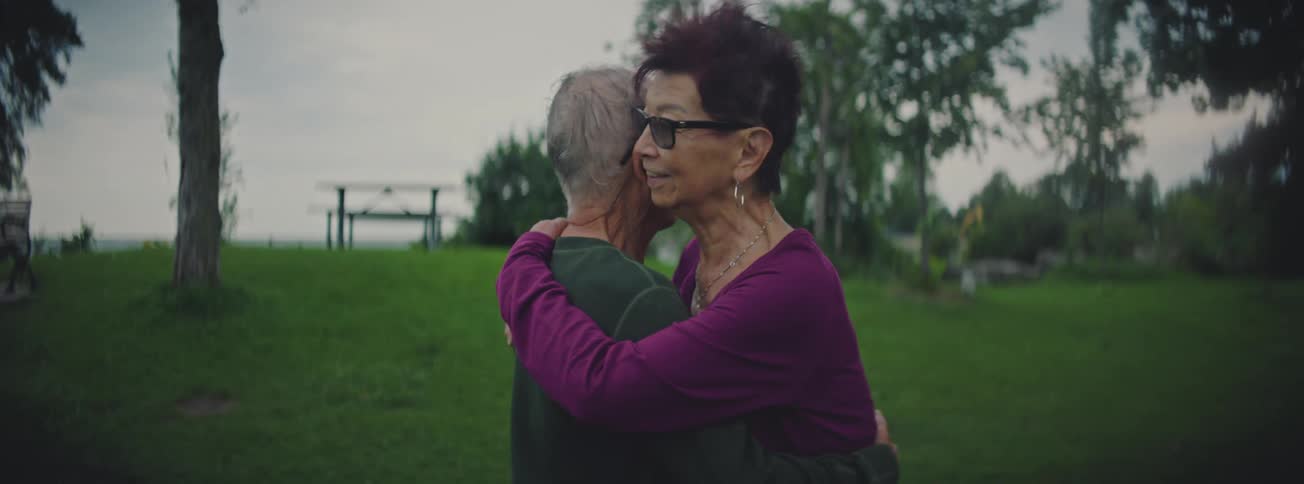 An elderly couple shares a long, loving embrace in a park in slow motion
