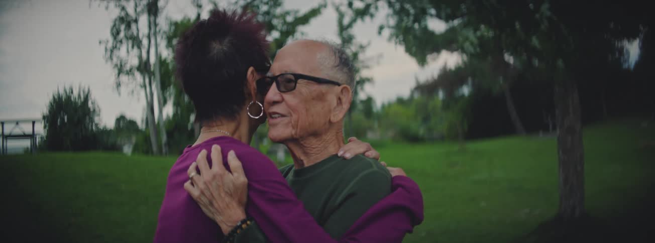 An affectionate elderly Asian couple embraces and slow dances together in a park during a tender moment