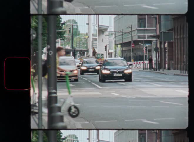 Vintage film-style footage captures the motion blur of cars, pedestrians, and scooters at a busy city intersection