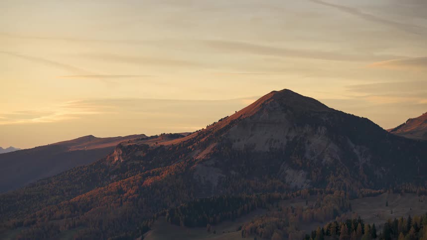 A lone mountain peak stands tall, bathed in the warm, golden light of a serene sunset