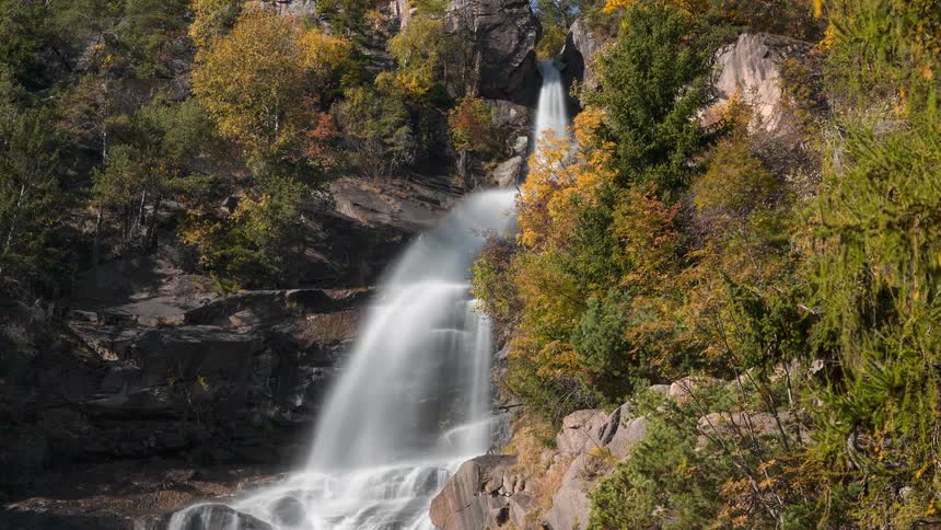 A beautiful long exposure timelapse of a waterfall cascading down a rocky cliff surrounded by colorful autumn foliage