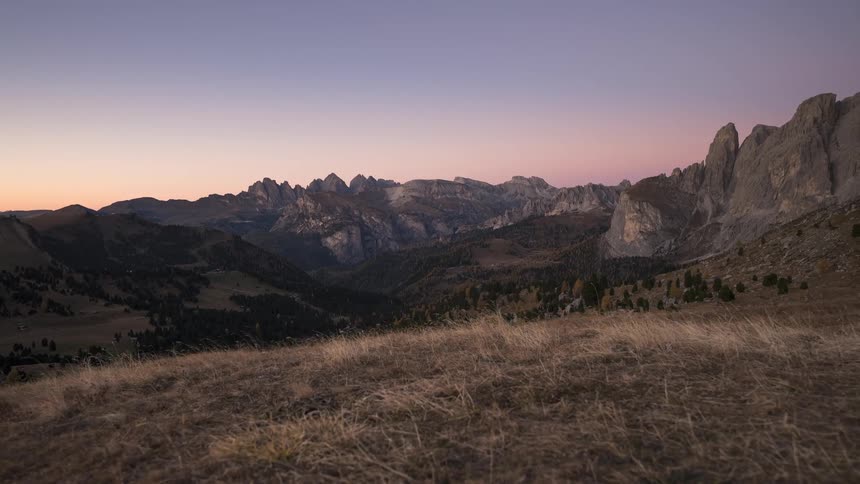 A breathtaking timelapse of twilight descending over a majestic mountain valley as the sky fades from orange to purple