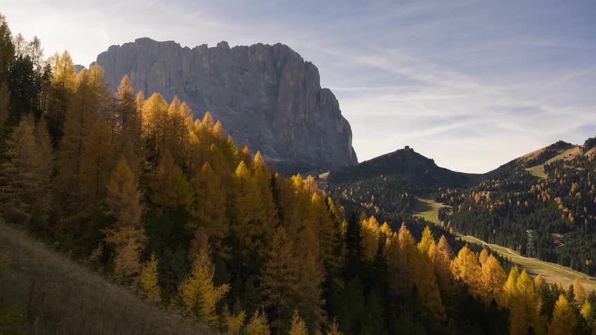 A stunning timelapse captures the changing light and moving clouds over golden larch trees and a rugged mountain peak in the heart of autumn
