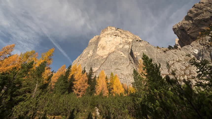 A majestic time-lapse of wispy clouds drifting over a towering mountain peak surrounded by vibrant yellow autumn trees