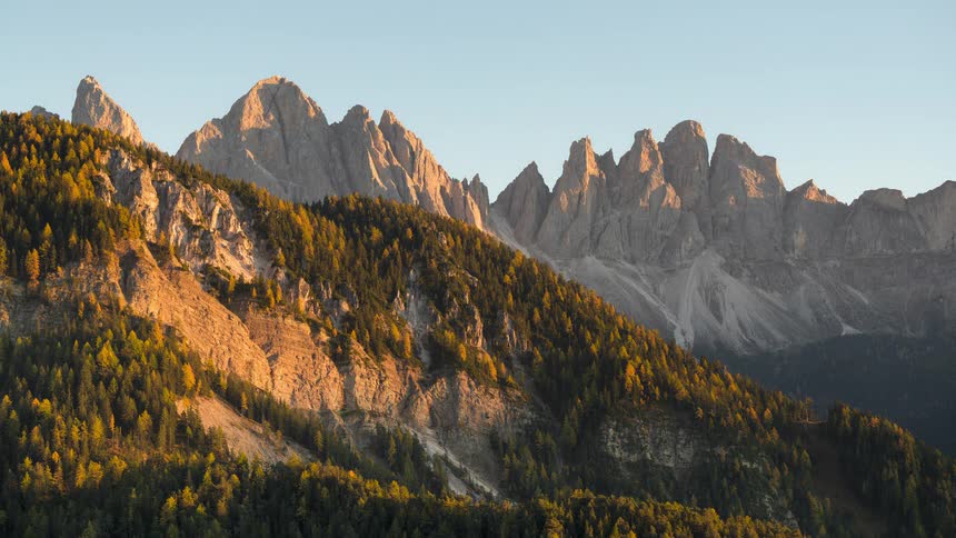 A beautiful sunset timelapse captures the golden alpenglow on the jagged peaks of the Dolomites over a colorful autumn forest