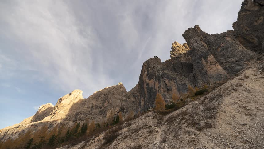 A dramatic timelapse captures clouds moving swiftly over rugged mountain peaks and a rocky slope during a sunny autumn day