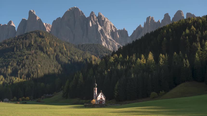 A timelapse of the iconic Church of St. John in Ranui as sunlight and shadows move across the green valley below the towering Dolomite mountains in Italy