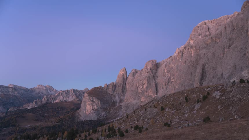 A serene timelapse captures the transition from a purple pre-dawn sky to morning light over the majestic Dolomite mountains