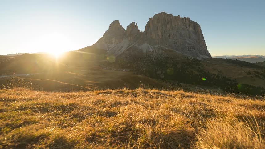 The sun rises over the iconic Sassolungo mountain in the Italian Dolomites, illuminating the golden autumn landscape