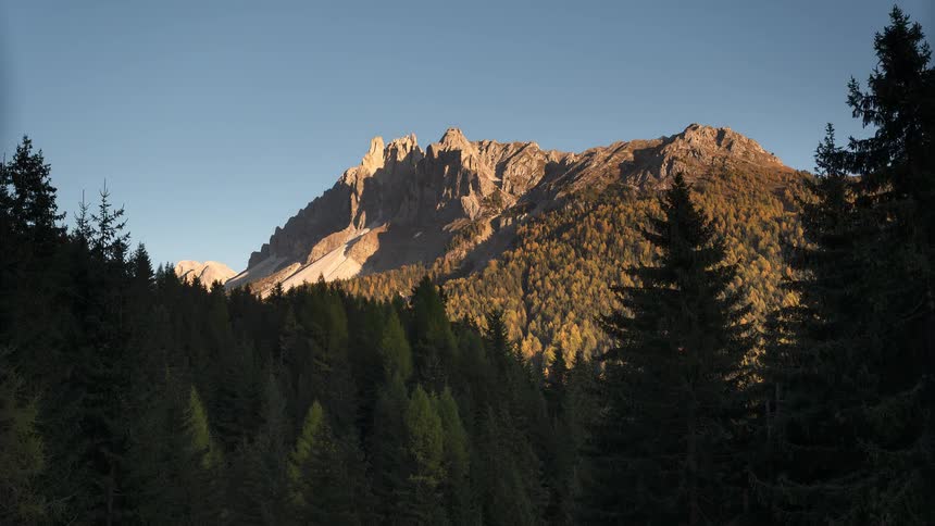 A beautiful sunset timelapse over a majestic mountain peak, with golden light sweeping across a lush autumn forest