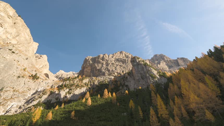 A time-lapse of a majestic mountain range with autumn-colored trees under a clear blue sky