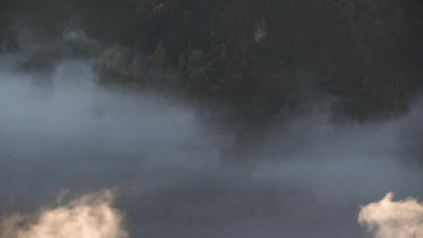 Ethereal time-lapse of dense fog and clouds swirling around and eventually enveloping a historic castle on a mountainside