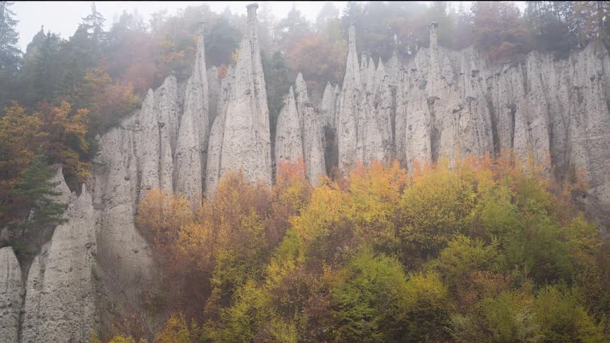 Unique geological earth pyramids stand majestically amidst a colorful autumn forest shrouded in morning fog