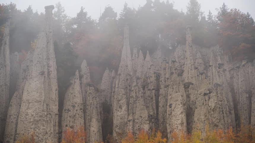 A mystical view of the Ritten Earth Pyramids rock formations shrouded in thick fog on a colorful autumn day in the Italian Dolomites