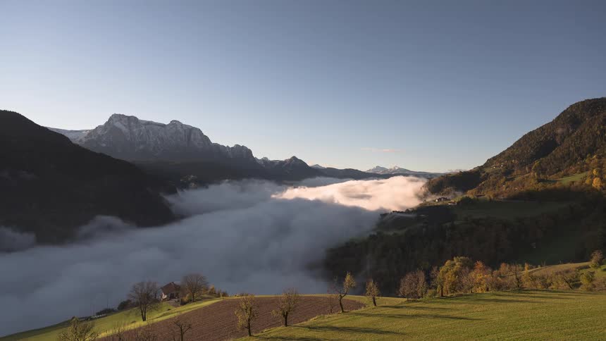 Morning light illuminates a river of fog flowing through a scenic mountain valley in this beautiful timelapse