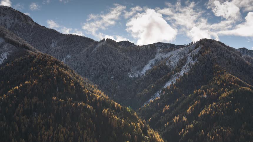 Timelapse of clouds drifting over a stunning mountain landscape where golden autumn trees transition to snow-dusted peaks