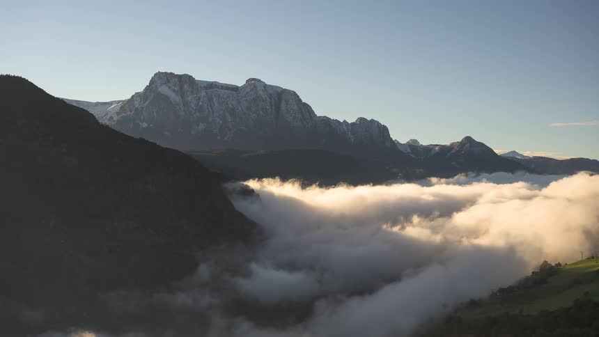 A stunning time-lapse of clouds flowing like a river through a sunlit valley below snow-capped mountains