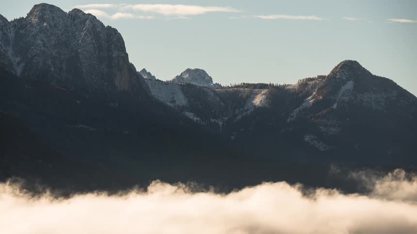 A stunning time-lapse captures a sea of clouds rolling through a valley beneath majestic, snow-dusted mountains