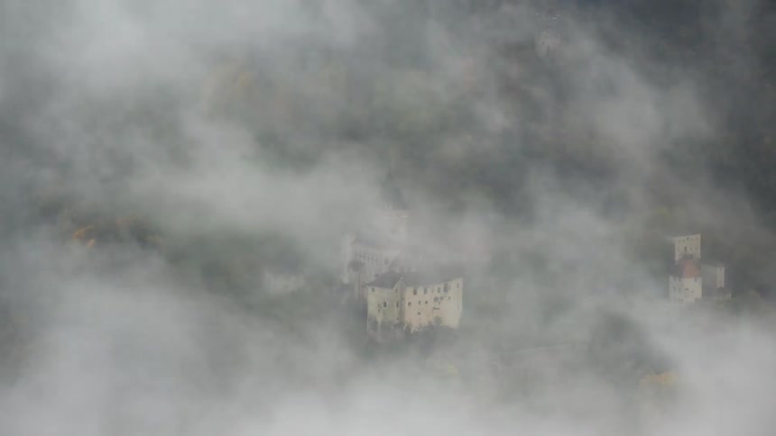 A mysterious European castle nestled in a forest is completely consumed by a thick blanket of fog