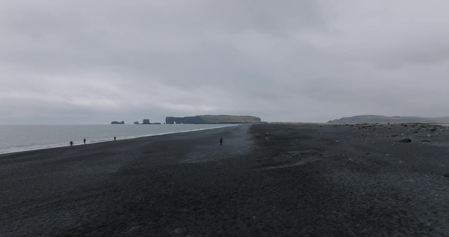 A slow aerial drone shot advances over the expansive black sand beach in Iceland on a cloudy day