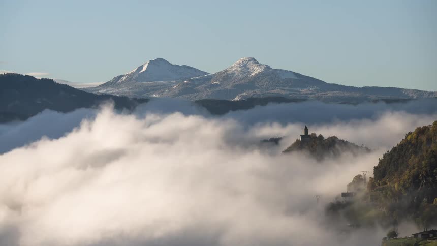 A mesmerizing time-lapse of a sea of fog rolling through a valley, revealing a hidden castle with snow-capped mountains in the background