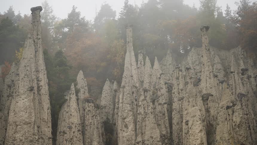 Unique geological earth pyramids stand tall against a dense forest backdrop on a very foggy and misty autumn day
