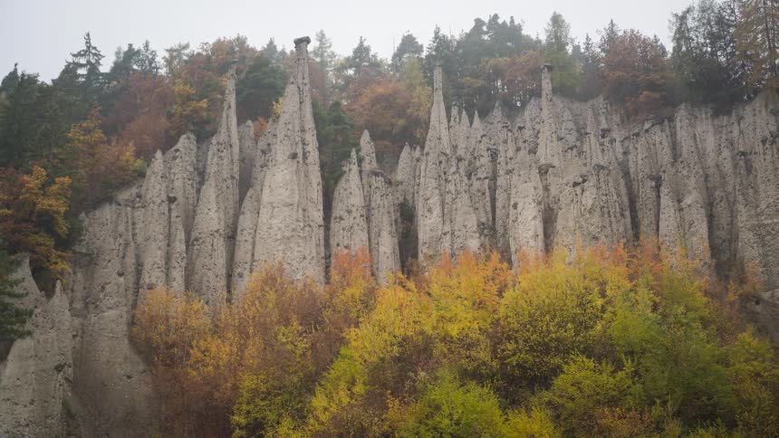 Majestic earth pyramids rise from a vibrant, misty autumn forest on a mountainside