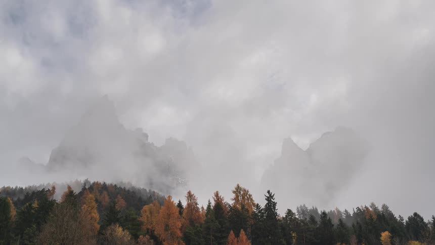 A time-lapse of dense fog and clouds rolling over a majestic mountain range above a colorful autumn forest