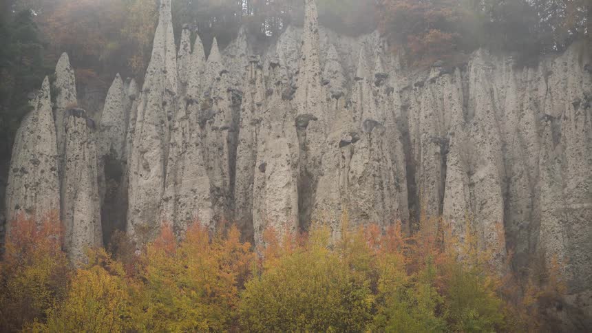 A slow zoom out reveals the unique Earth Pyramids of Platten in Italy, surrounded by a misty, colorful autumn forest