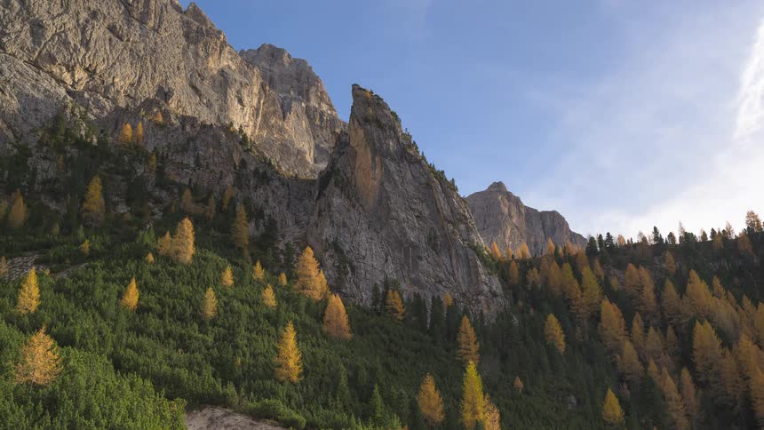 A scenic timelapse captures the majestic Dolomite mountains in autumn, with golden larches and shifting sunlight against a blue sky