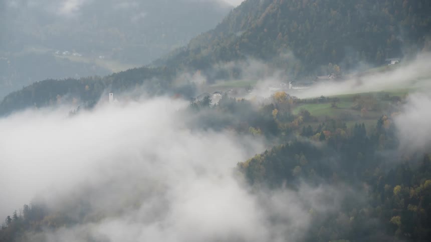 Morning fog and clouds dissipate in a time-lapse, revealing a beautiful Alpine village nestled in the mountains