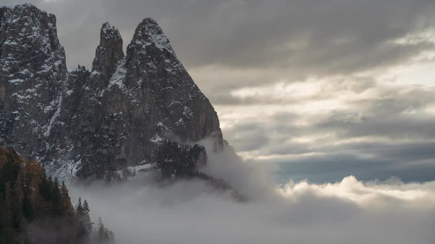 A stunning timelapse of thick, fast-moving clouds swirling around the base of a majestic, snow-covered mountain